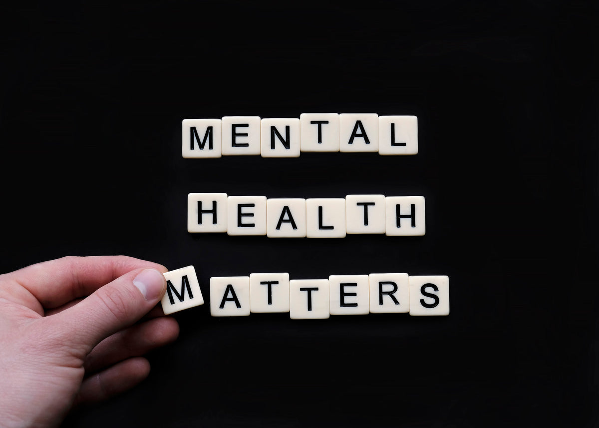 Tiles spelling 'mental health matters' on black surface with hand placing letter